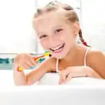 Girl smiling brushing her teeth at bathroom sink