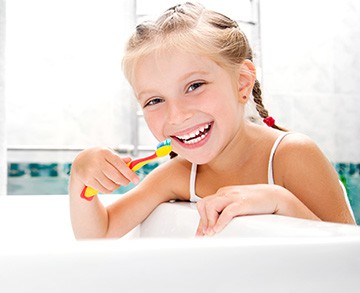 Girl smiling brushing her teeth at bathroom sink