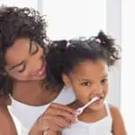 mother brushing her daughter's teeth in mirror