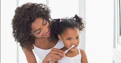 mother brushing her daughter's teeth in mirror