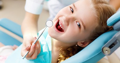 smiling girl in chair receiving a dental exam