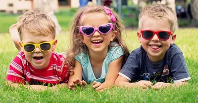 three children lying in grass wearing sunglasses