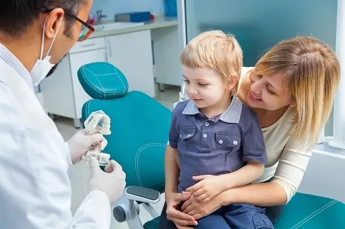 Little boy sitting with his mother on dental chair talking with dentist