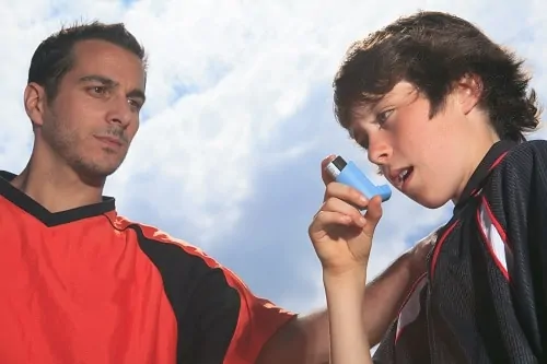 soccer player using his inhaler standing with his coach