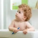 baby in sink holding toothbrush