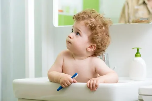 baby in sink holding toothbrush