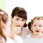 woman and little girl brushing teeth in mirror