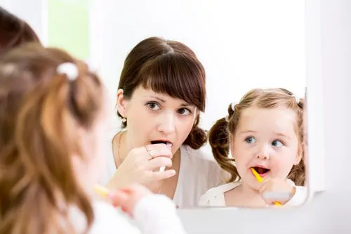 woman and little girl brushing teeth in mirror