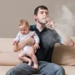 dad smoking cigarette with baby in his arms