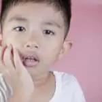 little boy holding mouth with toothache